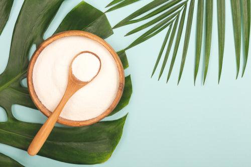 Wooden bowl of powdered supplement with spoon on tropical leaves background