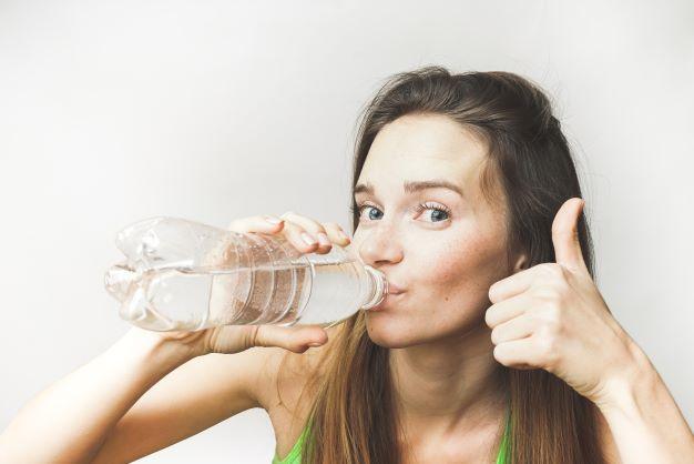 Woman drinking water from a plastic bottle and showing thumbs up, healthy lifestyle concept