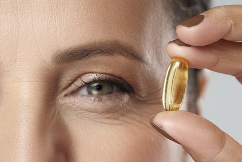 Woman holding a yellow supplement capsule near her face, close-up
