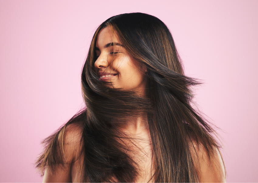 Smiling woman with healthy, shiny long hair against a pink background